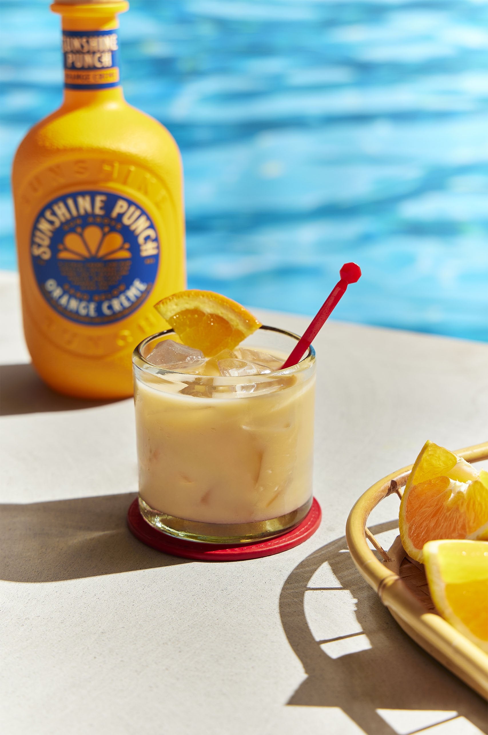 Glass of orange cream on ice with a bottle of Sunshine Punch by a pool.