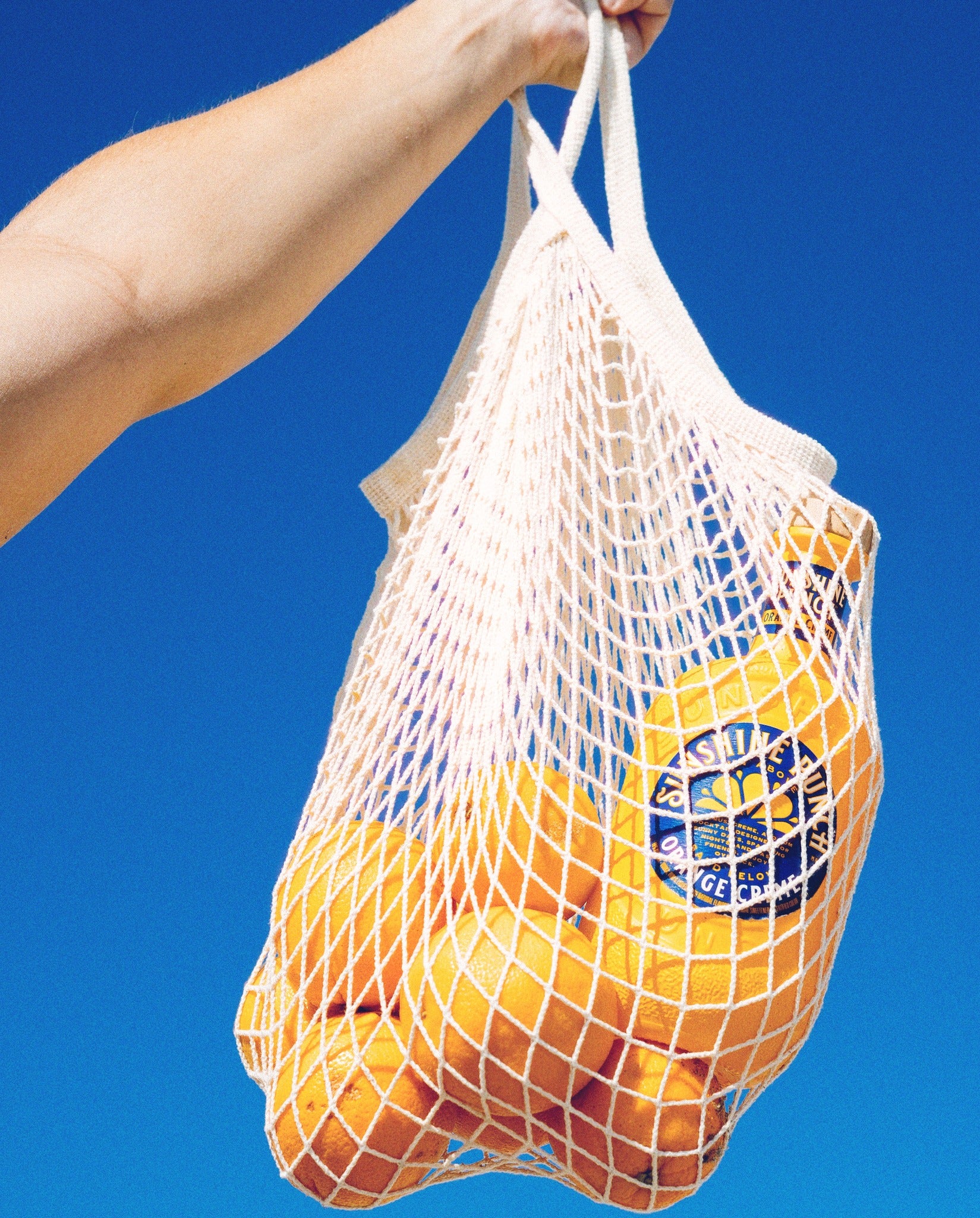 Net bag filled with oranges and Sunshine Punch against a blue background
